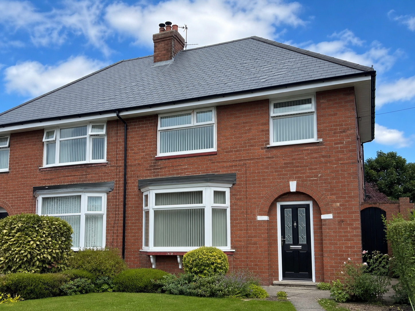 Completed natural slate re-roof on a red brick semi-detached house with new white uPVC fascias and black guttering