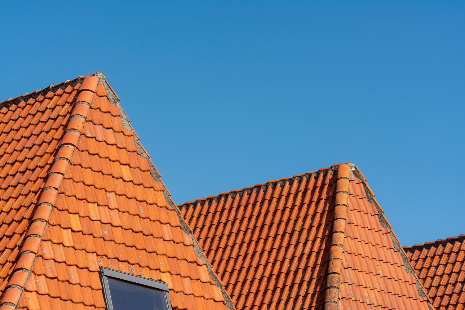 Newly finished orange clay tiled roof pitches with a fitted rooflight against a blue sky