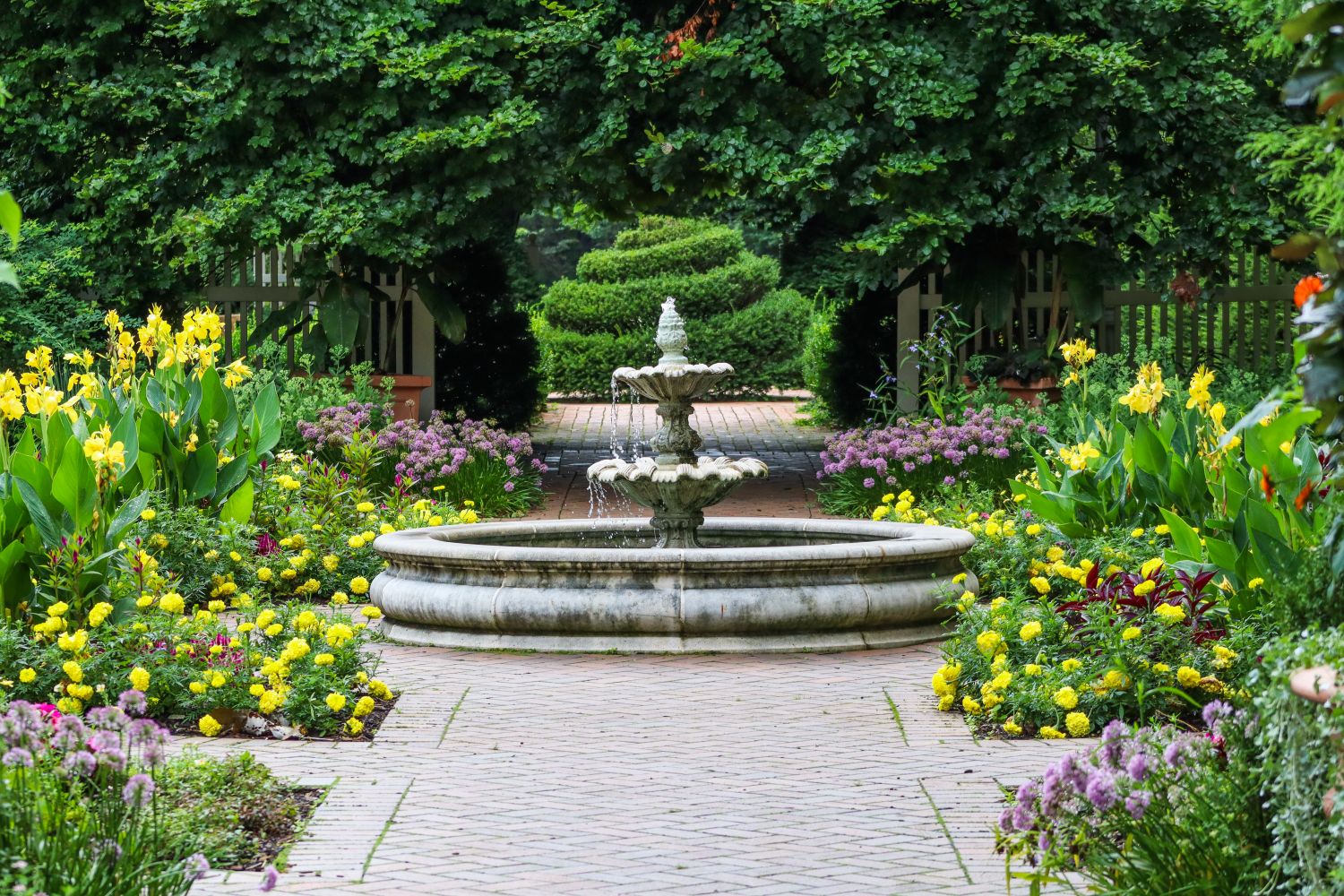 Traditional garden fountain surrounded by spring planting and a paved path