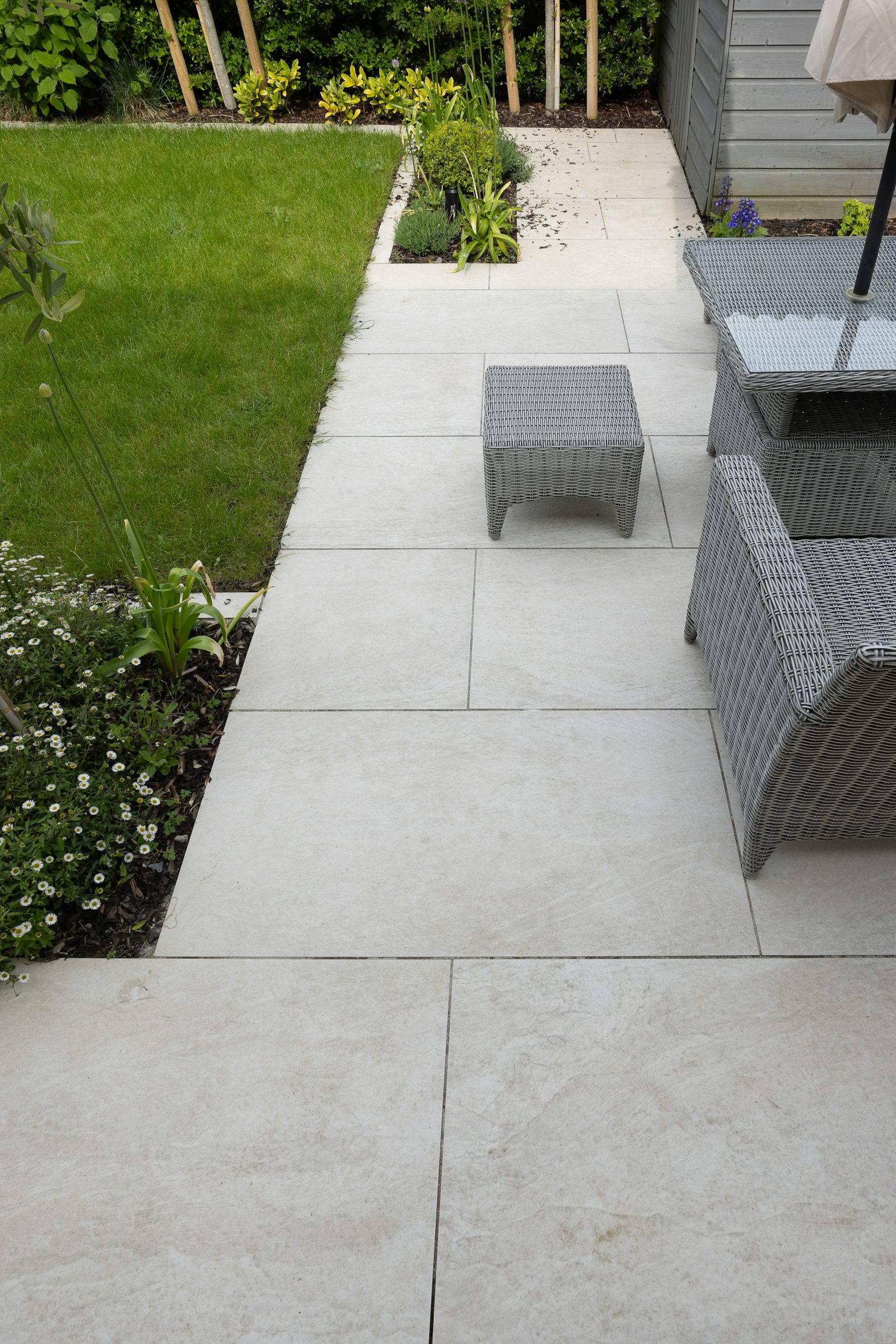 Newly laid light porcelain patio slabs with garden furniture beside a lawn